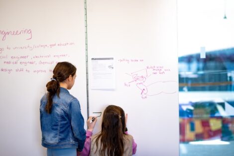 Two scouts write out their ideas on whiteboards inside a classroom.