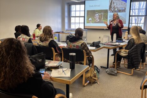 Susan Stifel teaches Girl Scouts Ambassadors about College. She stands in front of a presentation in a classroom.