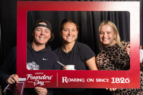 Three students hold a photo frame in a photo booth. The frame reads 