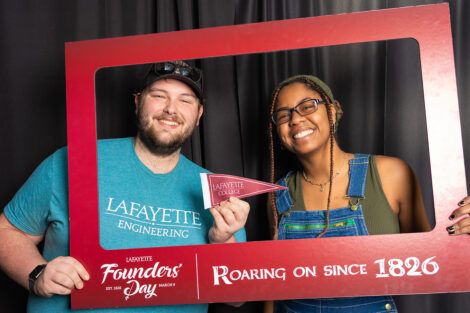 Two students hold a photo frame in a photo booth. The frame reads 