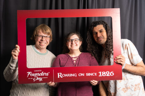 Three students hold a photo frame in a photo booth. The frame reads 