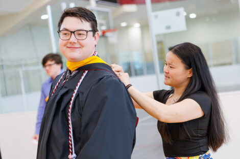 Students put on their caps and gowns with the help of fellow students and staff.