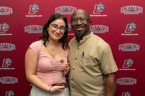 Francesca Stix ’25 and Professor Rexford Ahene stand and smile. Stix is holding a glass award.