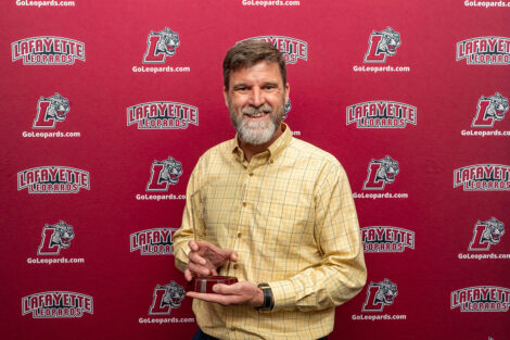 Trent Gaugler is holding a glass award and smiling at the camera.