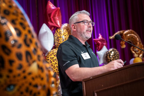 Benjamin Landis, senior director of annual giving is standing a a podium. Leopard balloons are in the background.