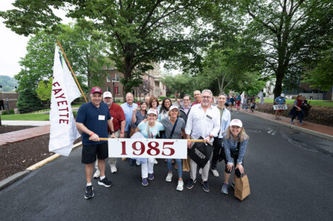 Members of the Class of 1985 hold a banner that reads 1985 at the parade.
