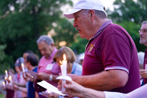 An alumnus is holding a candle and singing.