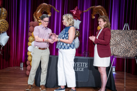 John Mulcahy ’87, P’27, vice president of the alumni association board, presents an award to Wynn Whitman '86. President Nicole Hurd looks on and claps.