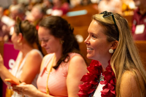 A close up of an alumna wearing a maroon flower lei is smiling.