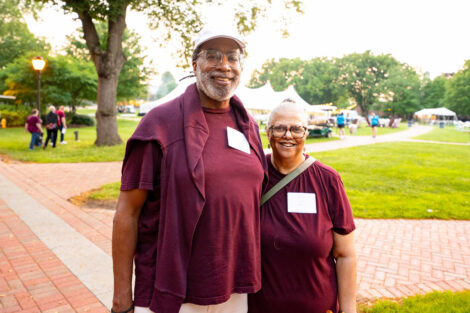 Two alumni are standing on the Quad. They are both wearing maroon.