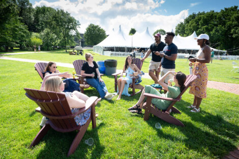 A group of alumni are sitting in chairs and standing on the Quad