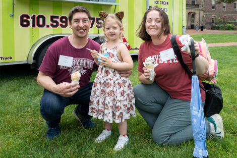 A couple are standing with their child near an ice cream truck on the Quad.