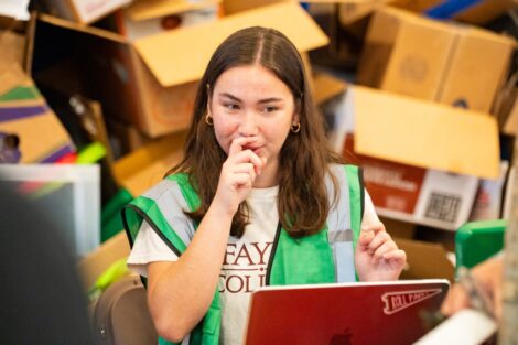 A volunteer wearing a Lafayette shirt and green vest works on a computer.