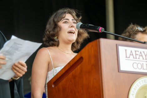 Isabella Crapanzano '26 sings from a podium on stage.