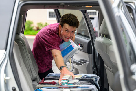 A student gathers clothes on hangers from the inside of a vehicle.