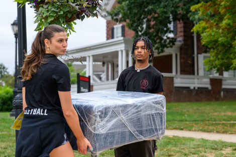 Students carry a large piece of furniture into a residence hall at Lafayette College.
