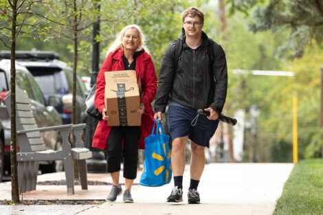 A student walks next to their family member, who carries a box.