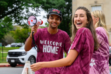 A student wearing a Welcome Home tshirt smiles with a megaphone.