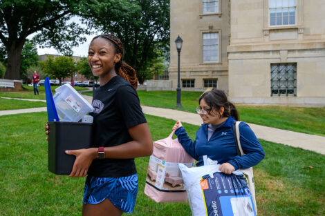 Two students smile as they carry in pillows and containers.