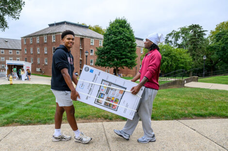 Two students carry a refrigerator through campus.