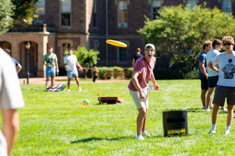 A student tosses a frisbee in front of Pardee Hall
