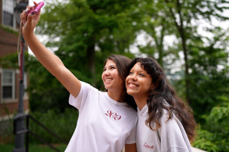 Two students take a photo together on an old digital camera in Bicentennial Abercrombie and Fitch clothing.