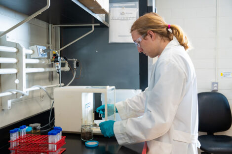 Owen Burry '27 stands in front of lab equipment spooning a brown substance onto a plate.