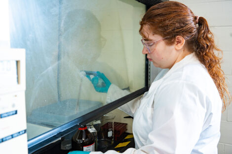 Emma Martin '28 stands extracts a liquid from a bottle under a lab ventilation hood