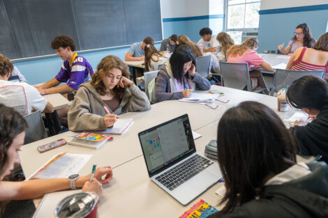 A large group of people are in a classroom and are writing intently on paper.