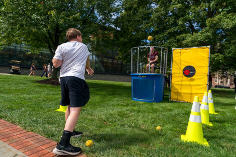 A child throws a ball at a dunk tank. The ball is mid-air.