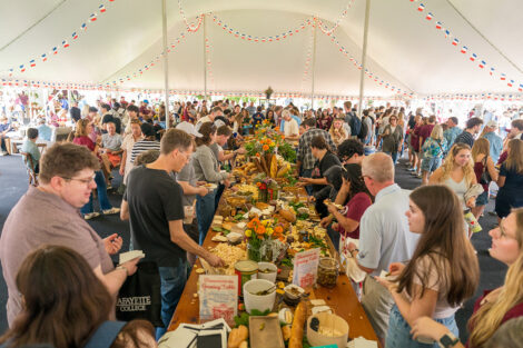 Guests enjoy food off of long wooden tables underneath a tent.
