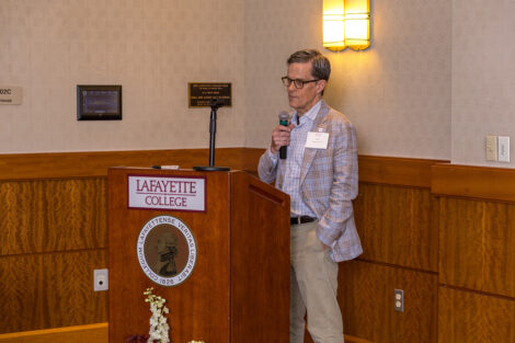 Parent John Mulcahy stands at a podium with a microphone at the Legacy Brunch.
