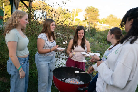 Attendees roast marshmallows over an outdoor charcoal grill.