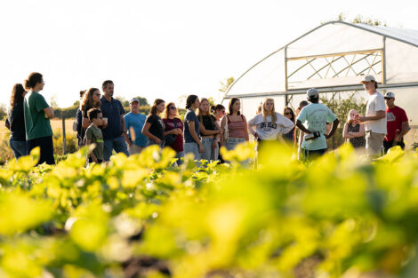 Attendees stand outside the greenhouse listening to a presentation on sustainability.