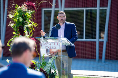 Head men's lacrosse coach Patrick Myers speaks during the dedication. He is standing at a podium.