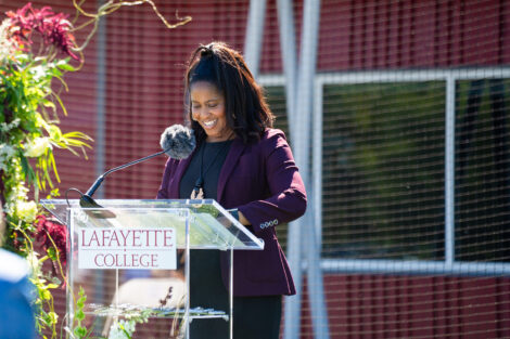 Director of Athletics Sherryta Freeman stands at a glass podium. She is wearing a maroon jacket.
