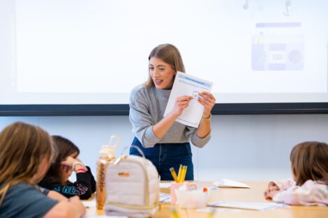 Prof. Lauren Biernacki holds up a sheet of paper as she teaches in front of a table of Girl Scouts.