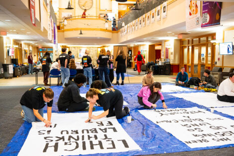 Students decorate a white sheet with blank paint for the Lehigh banners.