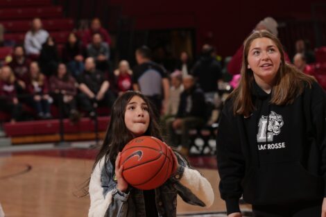 An EASD student holds a basketball, about to shoot a basket, with a women's lacrosse player next to her.