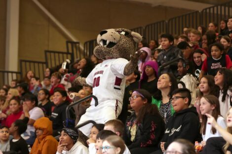 Roary the mascot reacts during the School Day Game, as he stands in the bleachers with students around him.