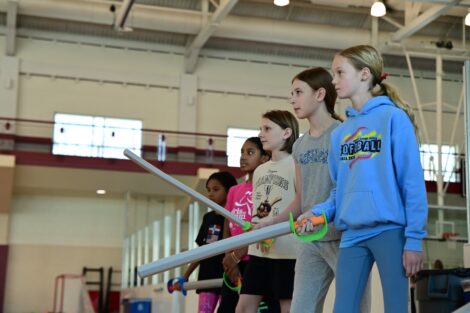 5 young participants hold foam swords as they try fencing.