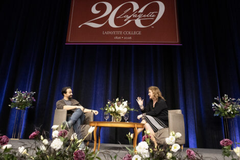 Lin-Manuel Miranda and President Nicole Hurd sit under a 200 banner in Kamine Gym.