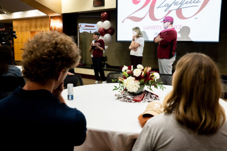 Prof. Susan Averett speaks to an audience. President Hurd and baseball coach AJ Miller are standing next to her.