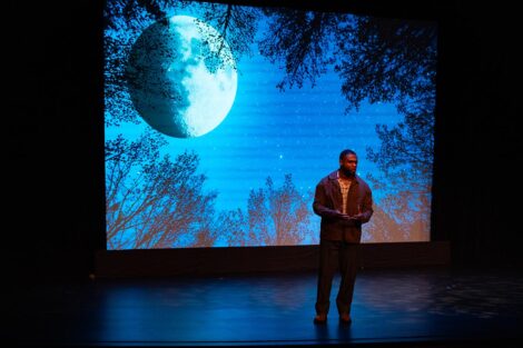 A person on stage in front of a projection of the moon