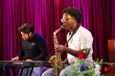 A person plays saxophone in front of another playing keyboards