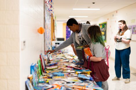 A Lafayette volunteer reaches across a table filled with books with EASD students nearby. The students look for books they'd like to take home with them.