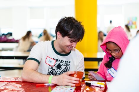 A Lafayette volunteer works with a student as she decorates a pot to hold a plant.