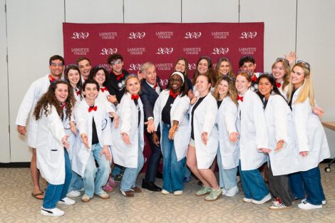 Students in lab coats post with Bill Nye