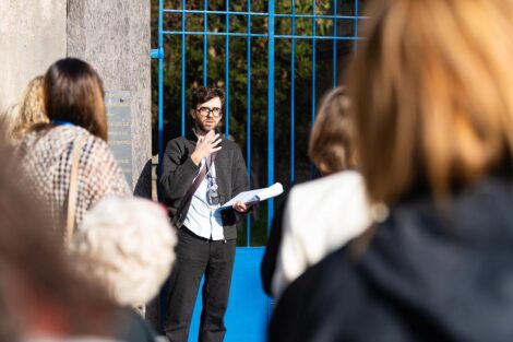 A guide presents in front of a blue gate in the cemetery.