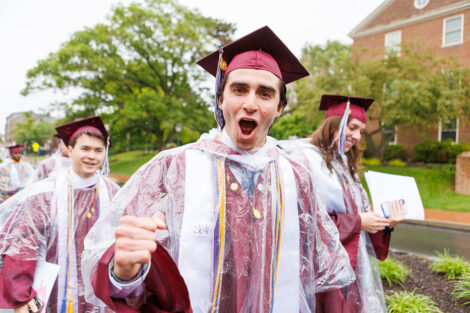 Students walk in graduation gowns and a poncho.